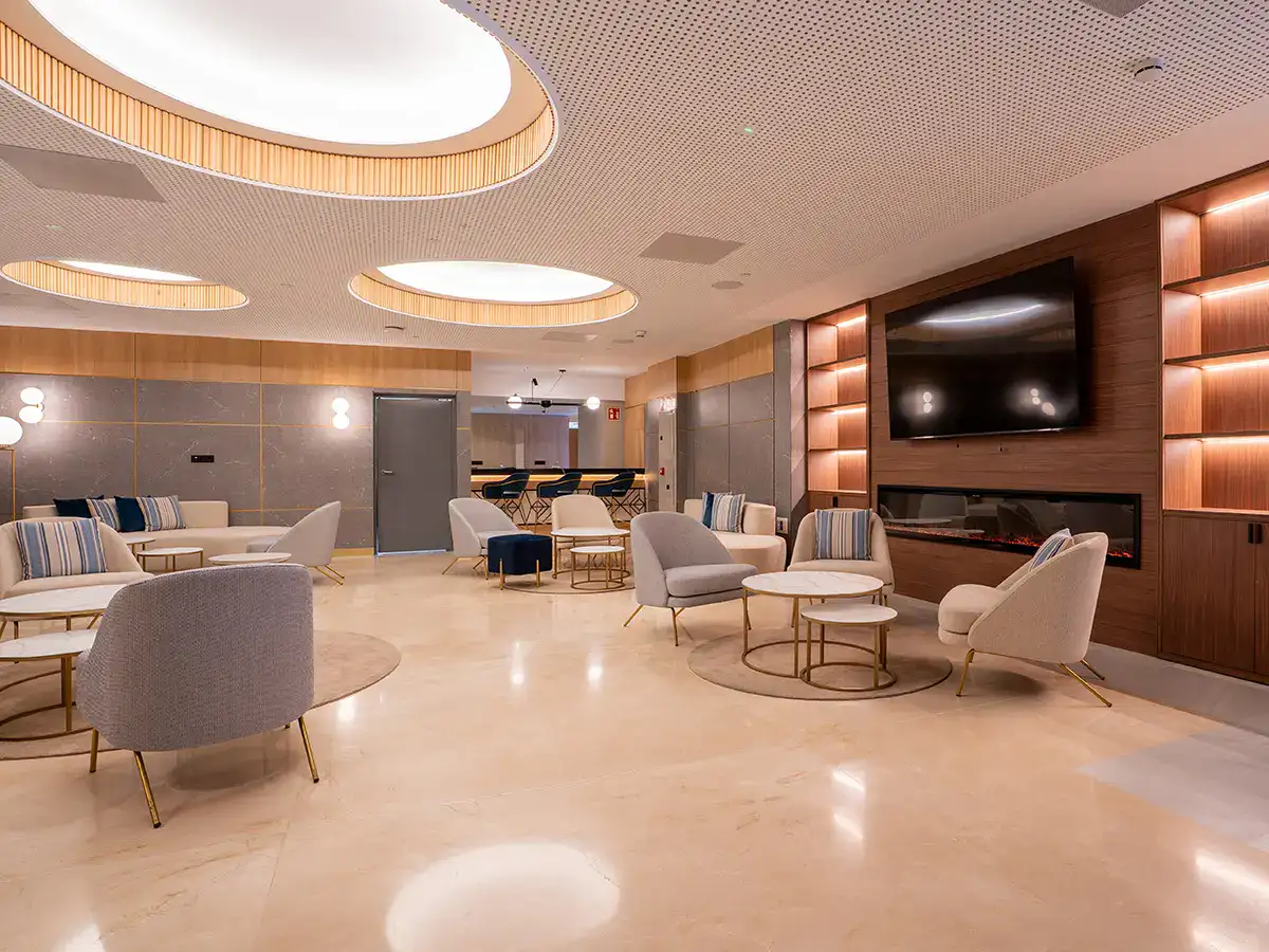 Sala moderna con sillones, mesas y luces circulares. TV en la pared.