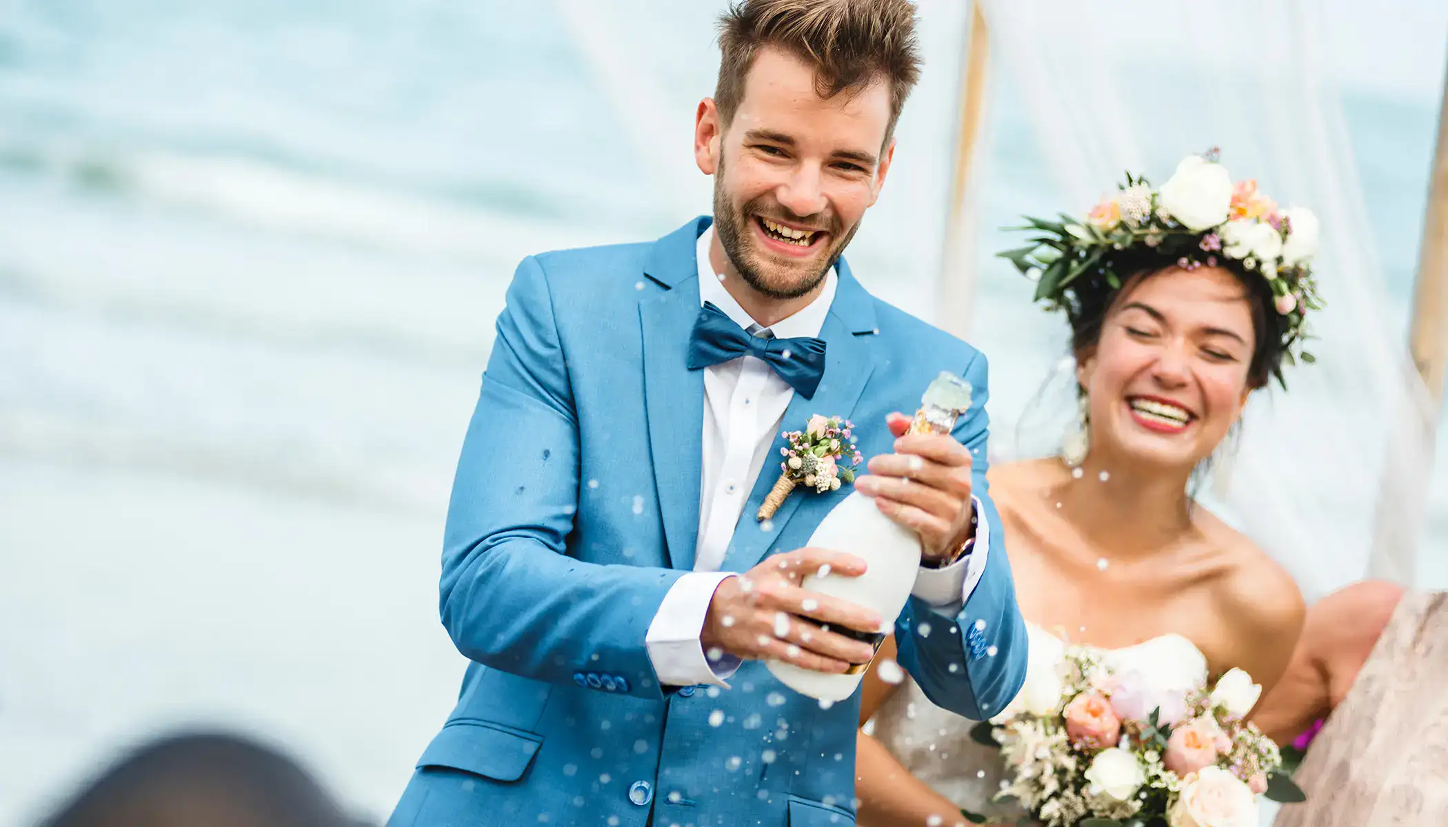 Pareja feliz celebrando en su boda con champ&aacute;n en la playa.