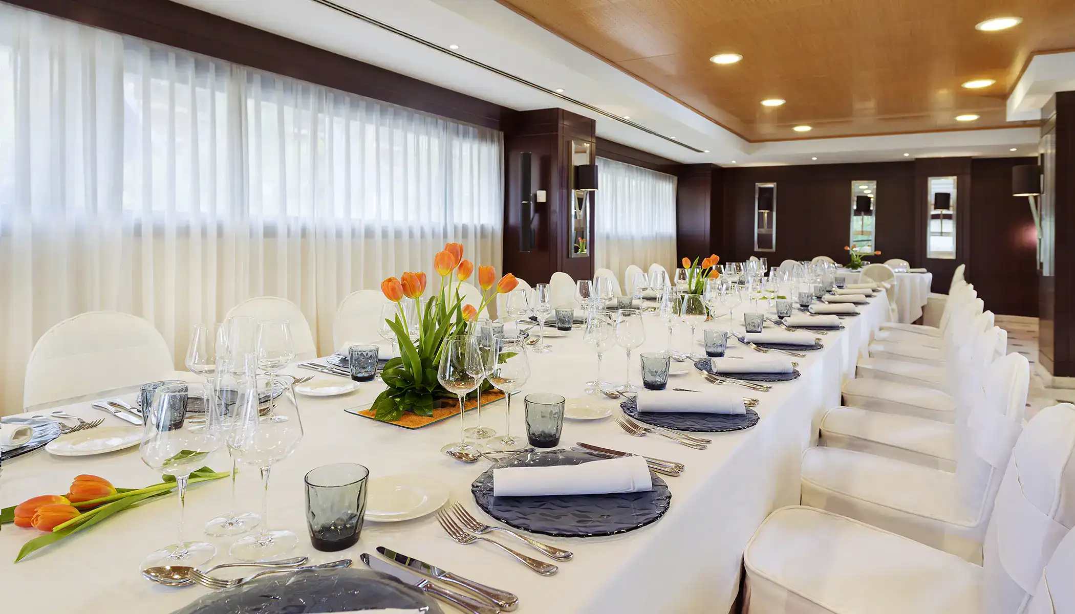 Mesa elegante decorada con tulipanes naranjas en sal&oacute;n iluminado.