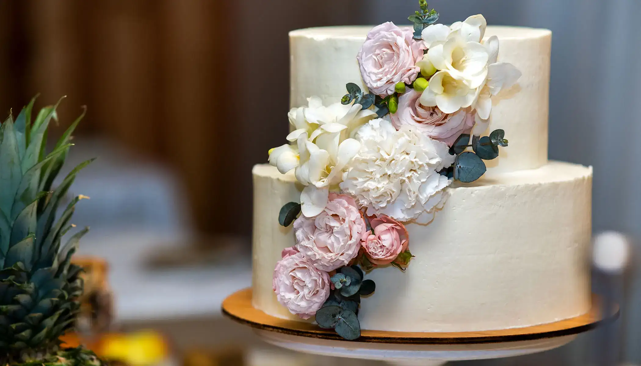 Pastel blanco de dos niveles con flores rosadas y blancas decorando un lado.