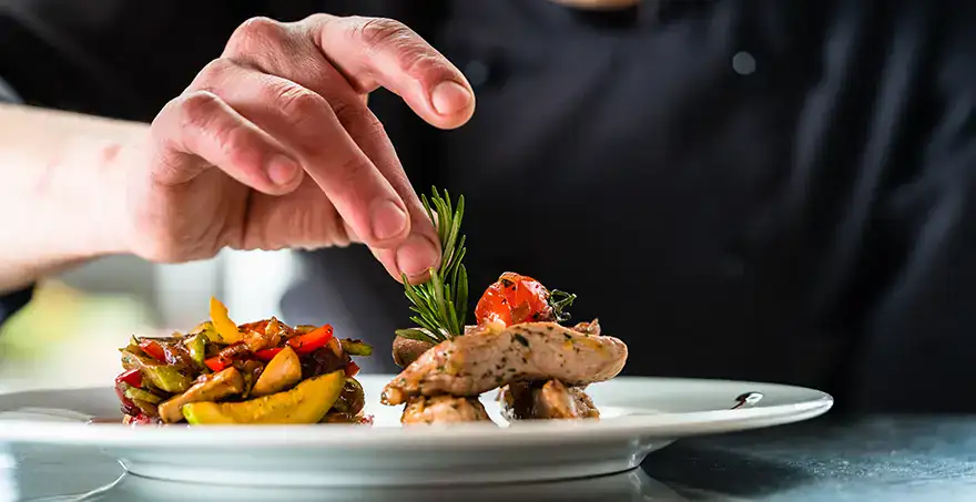 Chef decorando un plato gourmet con carne y guarnici&oacute;n de vegetales.