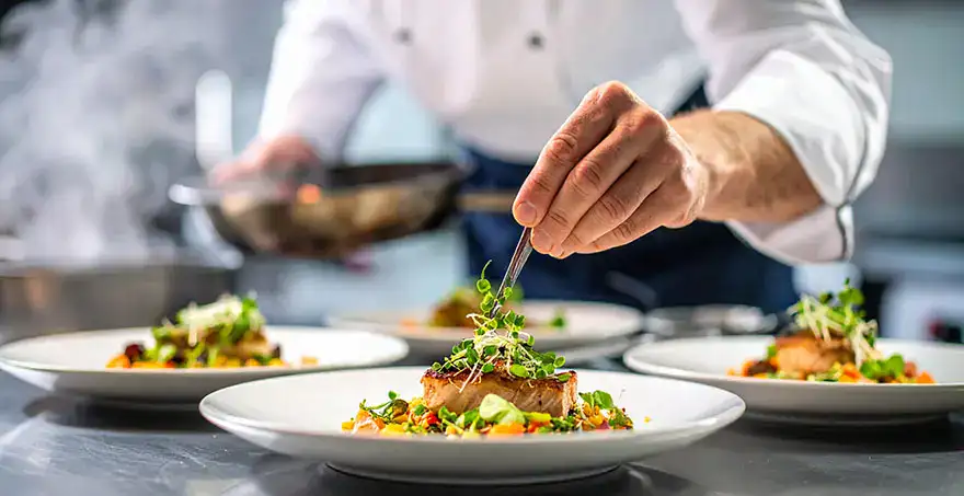 Chef decorando platos gourmet con hierbas frescas en una cocina profesional.