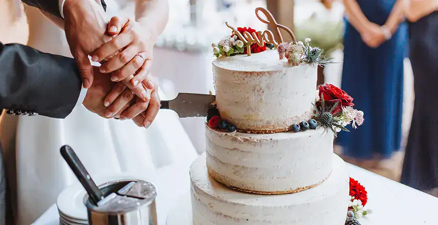 Pareja cortando un pastel de bodas decorado con flores y frutas.