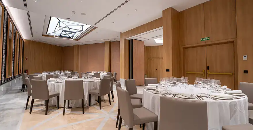 Sal&oacute;n elegante con mesas redondas, sillas grises y decoraci&oacute;n moderna.