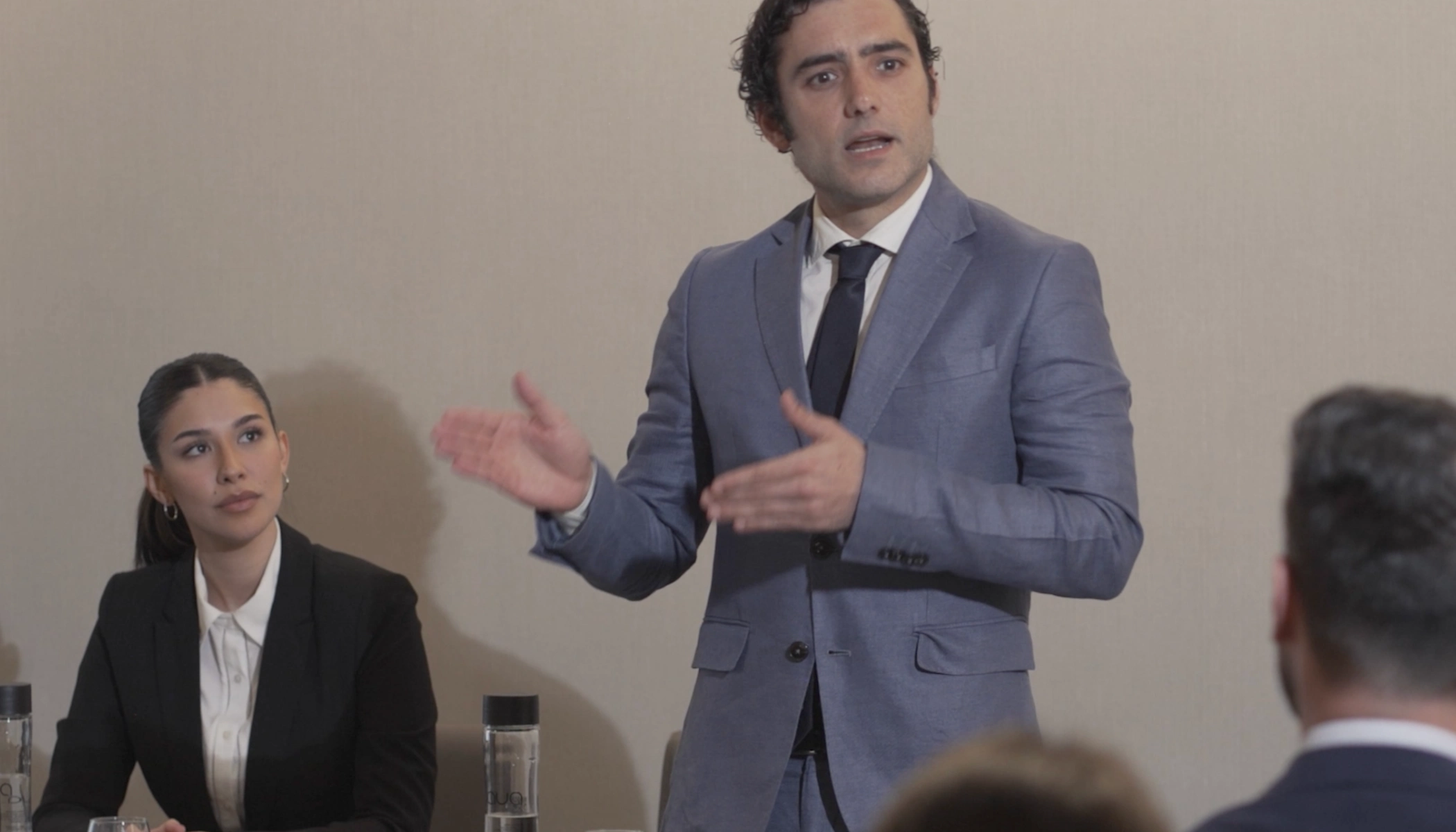 Un hombre presenta mientras una mujer atenta lo observa en una conferencia.