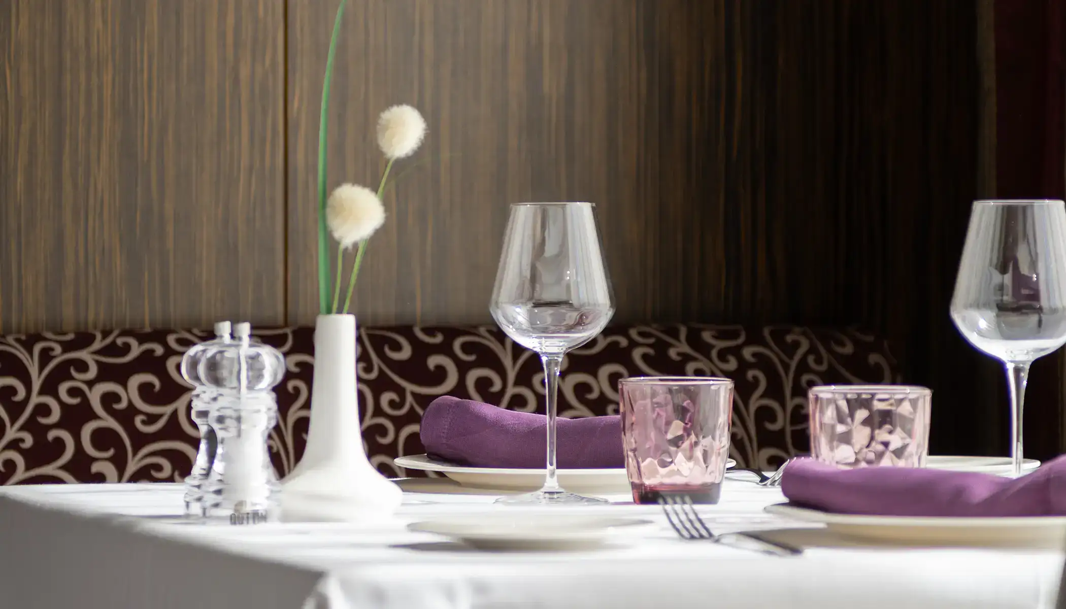 Mesa elegante con copas, servilletas moradas y florero blanco.