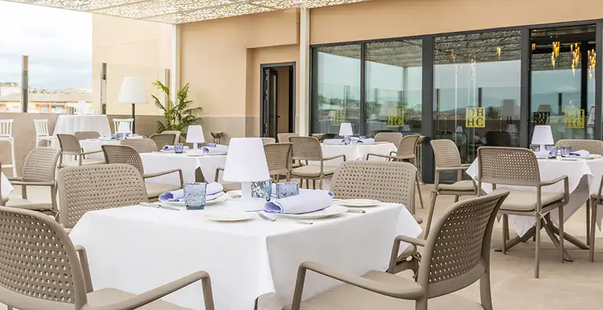 Terraza con mesas vestidas de blanco y sillas beige al aire libre.
