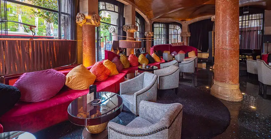 Elegante sal&oacute;n con sof&aacute;s rojos, cojines coloridos y mesas peque&ntilde;as.