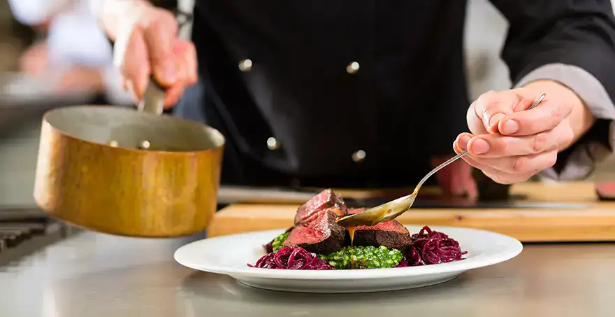 Chef emplata un platillo gourmet con carne y vegetales.