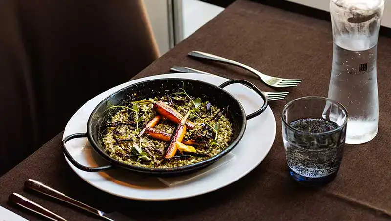 Plato de arroz con vegetales en sart&eacute;n sobre mesa con cubiertos y vaso de agua.