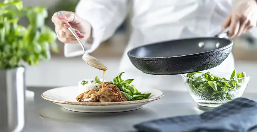 Persona sirviendo salsa sobre un plato con carne y vegetales.