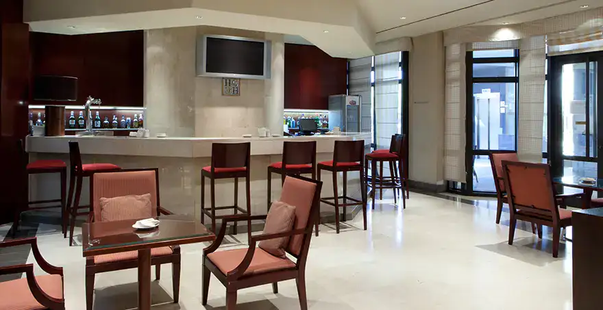 Bar elegante con barra y sillas altas, mesas y sillas en primer plano.