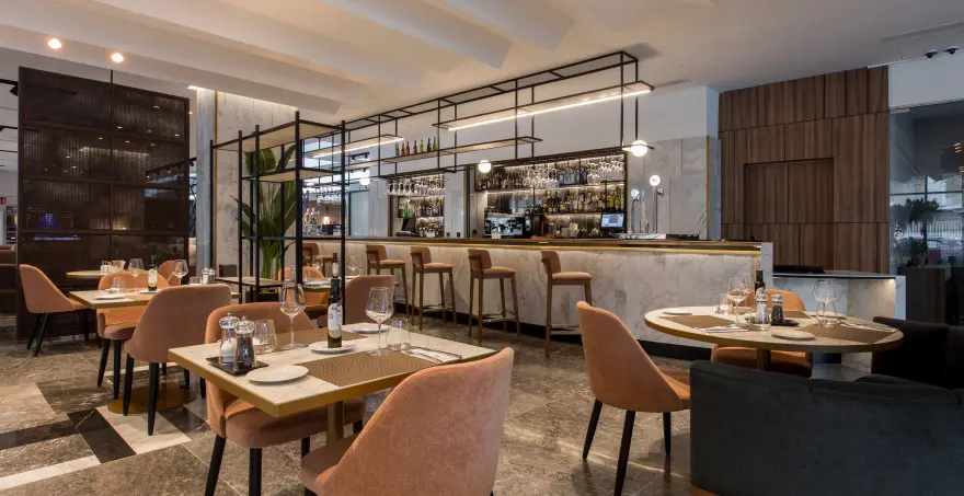 Restaurante moderno con mesas y sillas elegantes cerca de una barra iluminada.