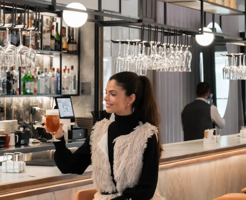Mujer sonriendo con vaso de cerveza en un elegante bar moderno.
