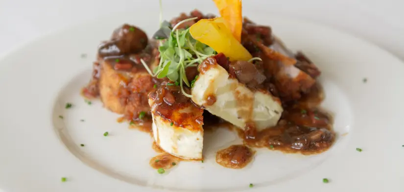 Plato gourmet con salsas, vegetales y guarnici&oacute;n verde en un plato blanco.