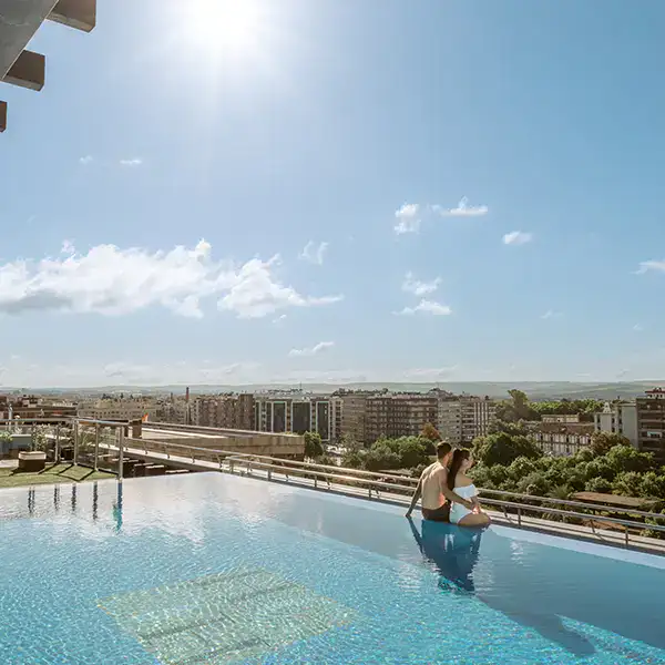 Pareja en una piscina en la azotea con vista a la ciudad en un d&iacute;a soleado.