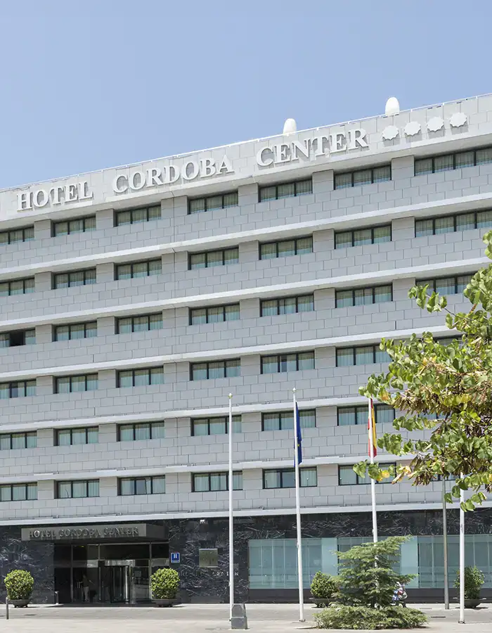 Fachada del Hotel C&oacute;rdoba Center con &aacute;rboles y banderas al frente.