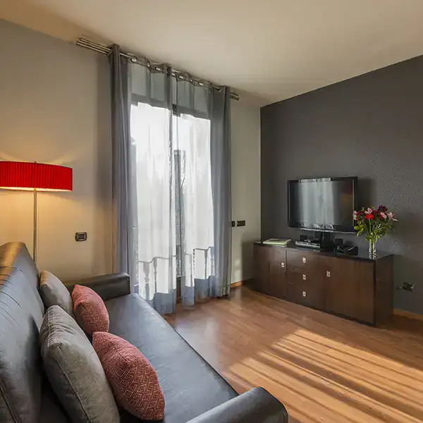 Sala de estar con sof&aacute;, l&aacute;mpara, televisor y decoraci&oacute;n simple.