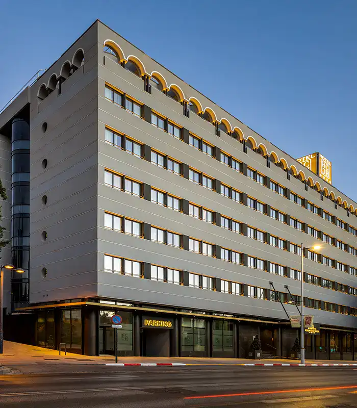 Edificio gris de cinco pisos con letrero de hotel y estacionamiento.