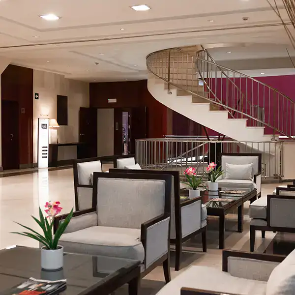 Sala de espera moderna con sillones grises y escaleras curvas.