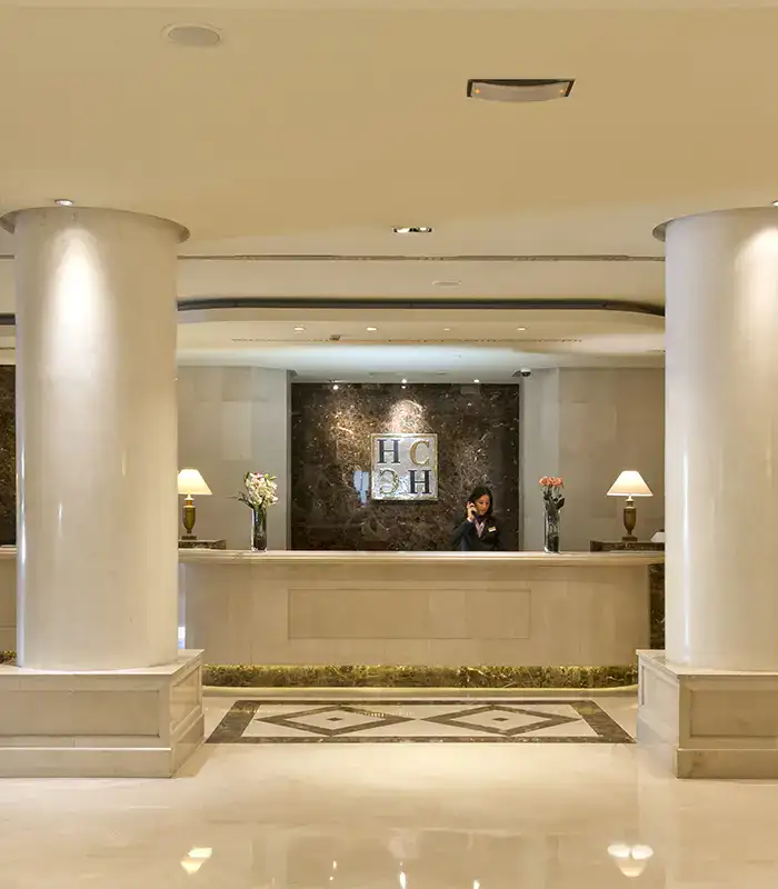 Recepci&oacute;n de hotel con columnas y un recepcionista al tel&eacute;fono.