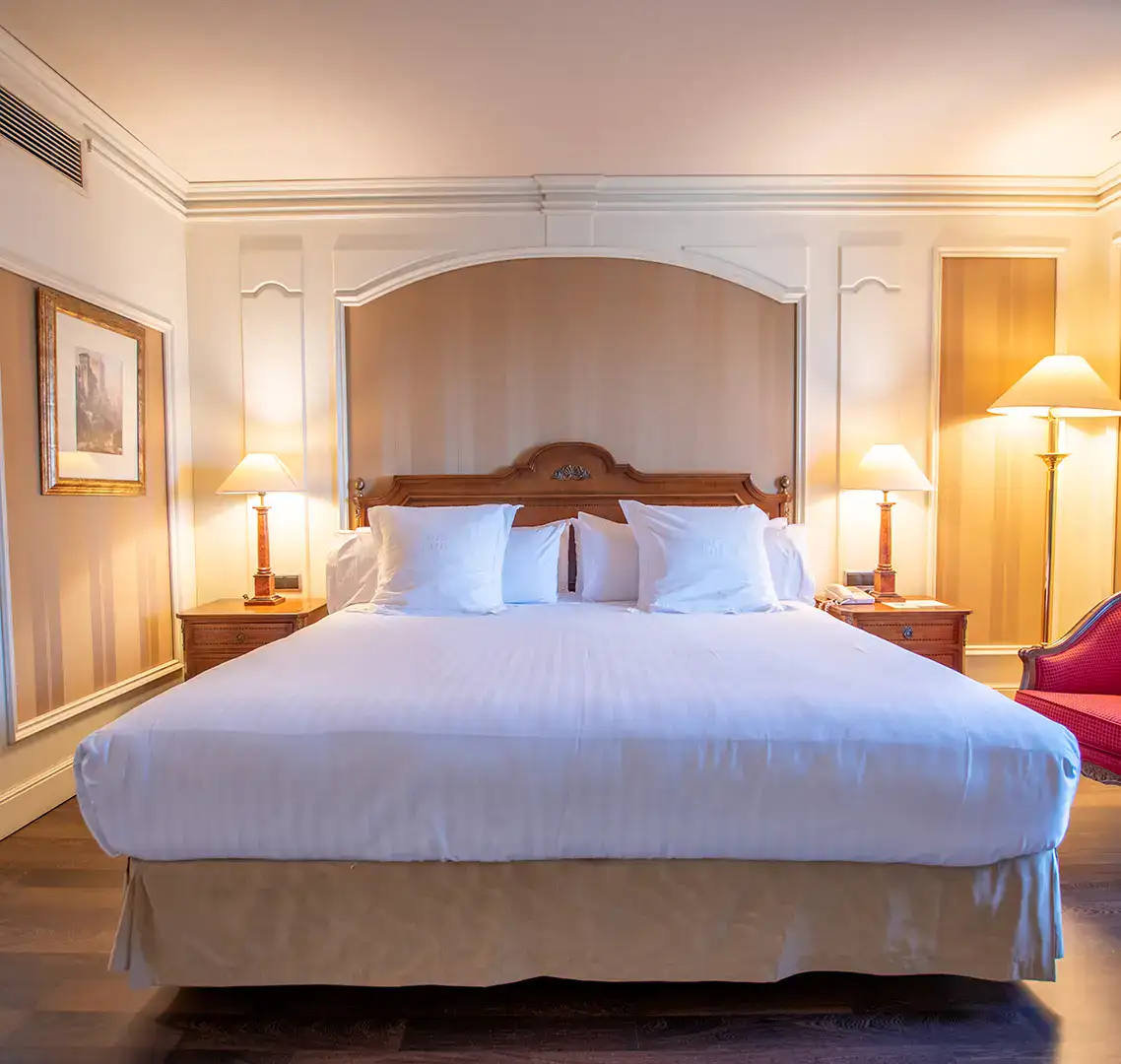 Cama con ropa blanca y l&aacute;mparas laterales en una habitaci&oacute;n elegante.