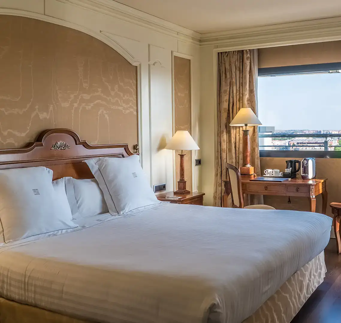 Habitaci&oacute;n de hotel con cama grande y mesa junto a una ventana.