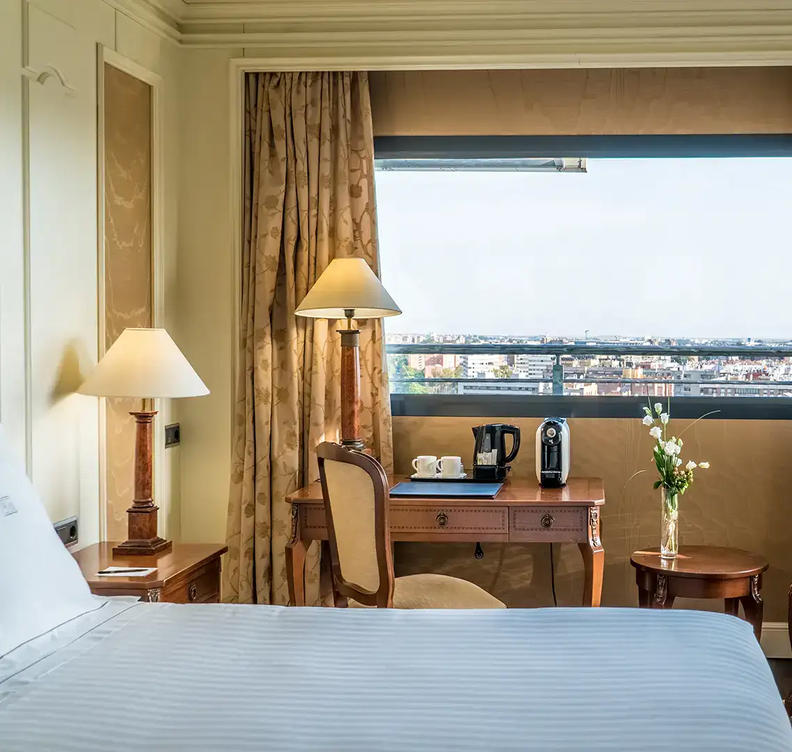 Habitaci&oacute;n de hotel elegante con vista a la ciudad a trav&eacute;s de una gran ventana.