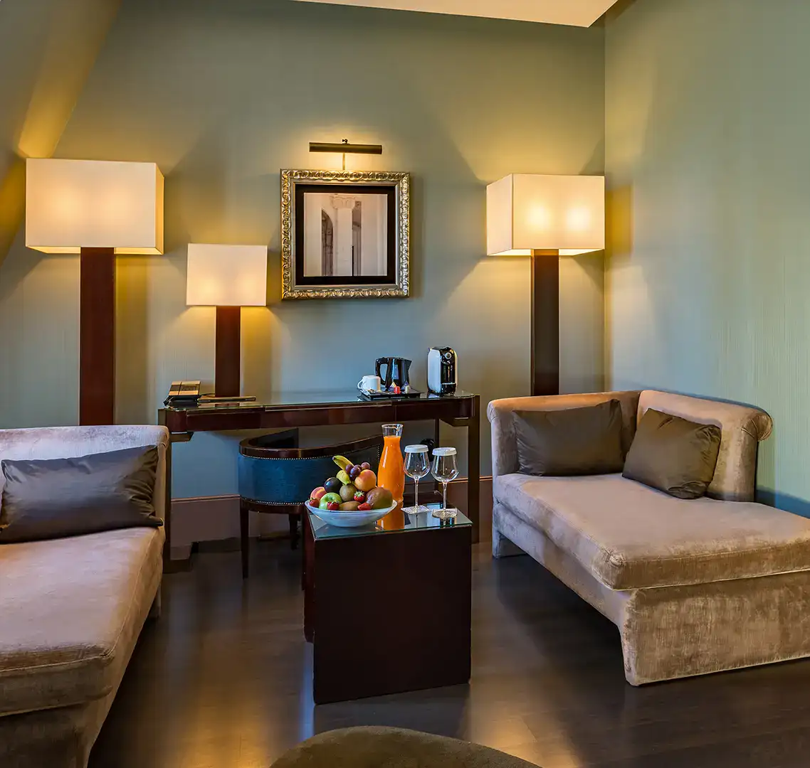 Sala acogedora con sillones, l&aacute;mparas, cuadro y mesa con frutas y bebida.