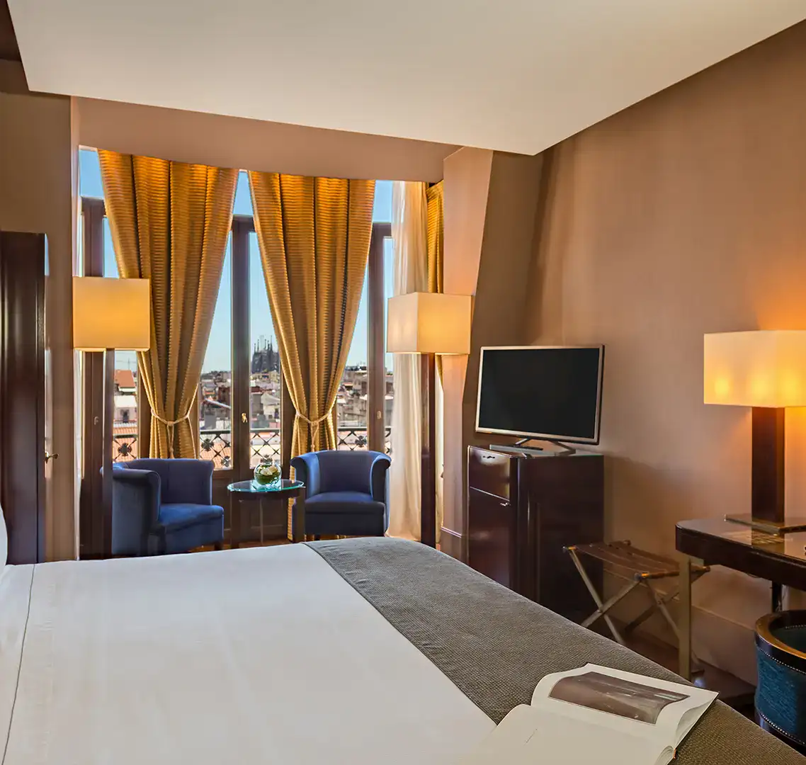 Habitaci&oacute;n de hotel luminosa con cama, televisor y vistas a la ciudad.