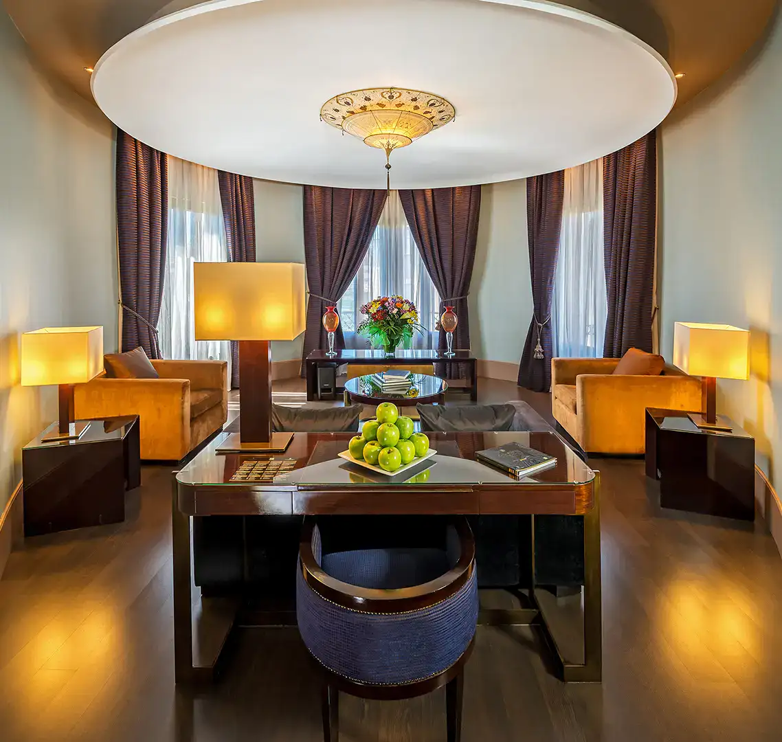 Sala elegante con mesa, manzanas verdes y sillones, bajo l&aacute;mpara de techo.