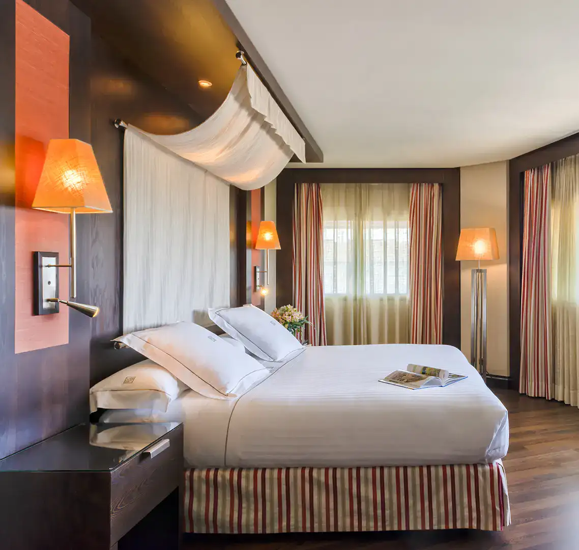 Habitaci&oacute;n con cama doble, l&aacute;mparas c&aacute;lidas y cortinas a rayas.