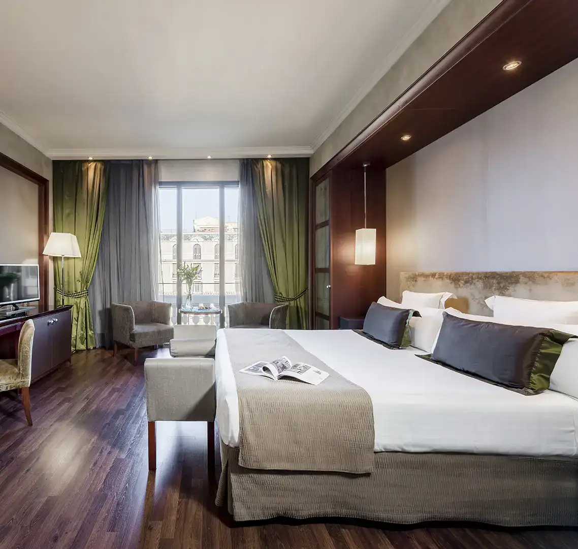 Habitaci&oacute;n moderna con cama grande y &aacute;rea de descanso junto a la ventana.