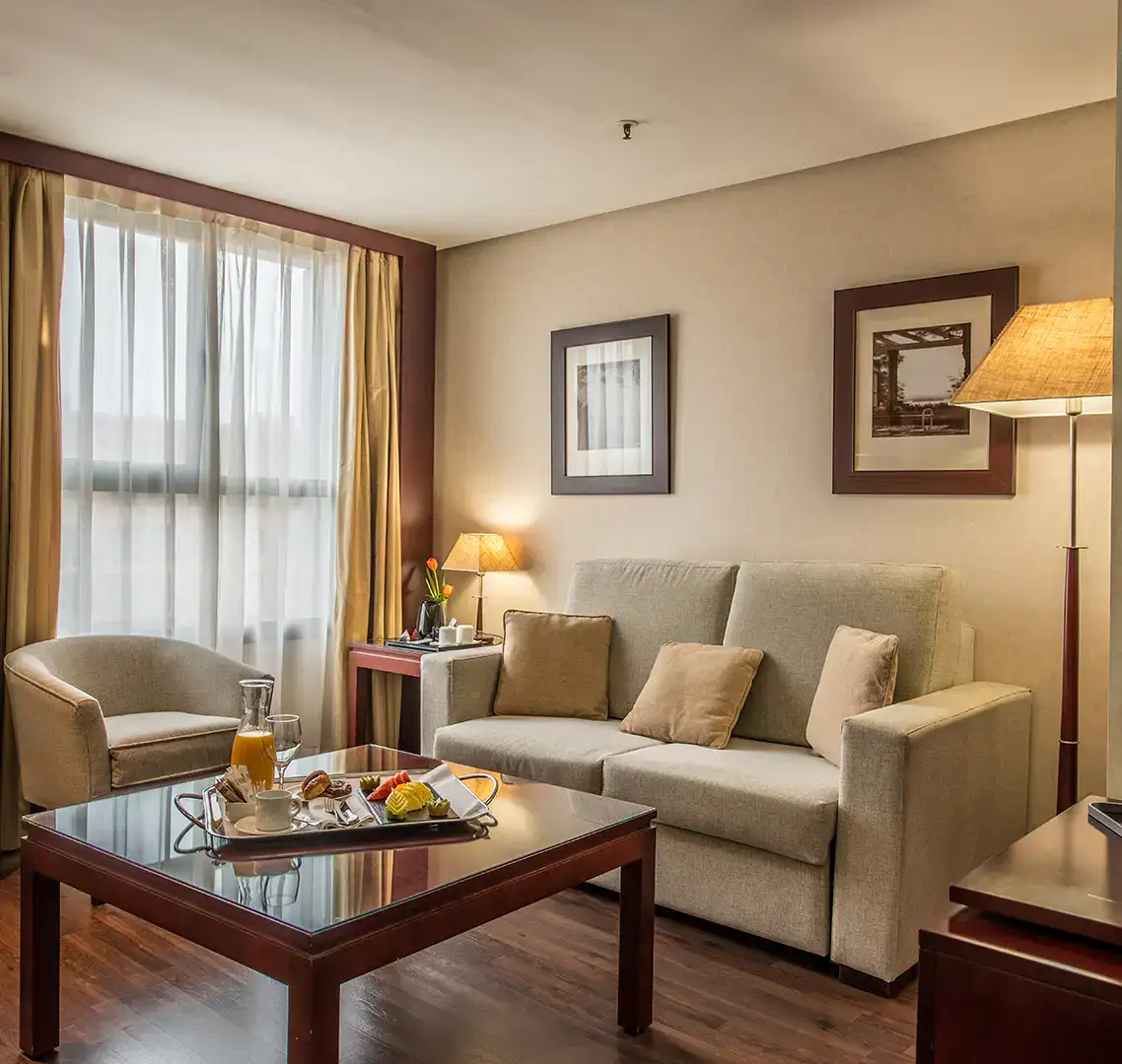 Sala de estar acogedora con sof&aacute; beige y mesa con desayuno.