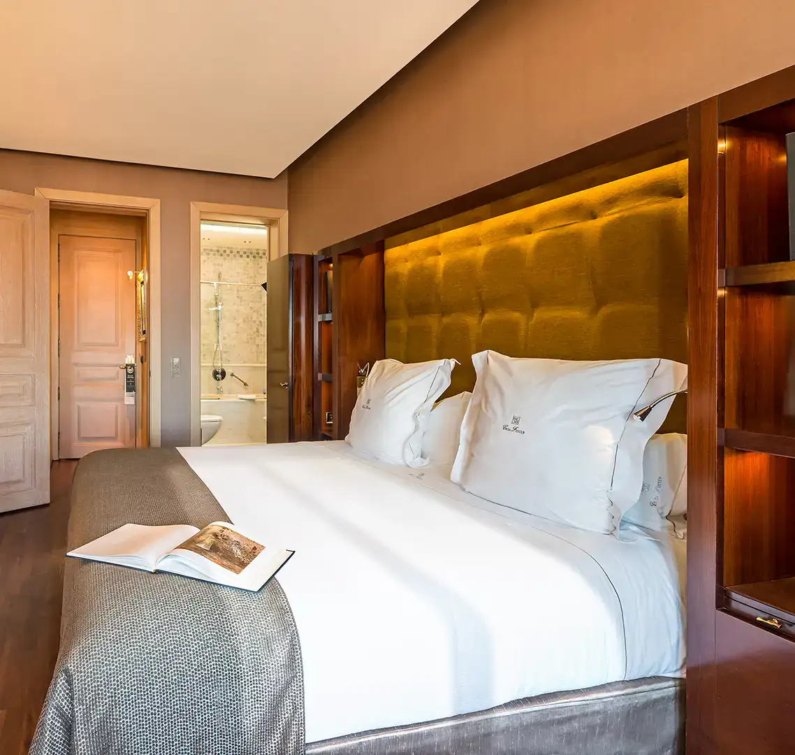 Cama de hotel con cabecero iluminado y libro abierto en la colcha.