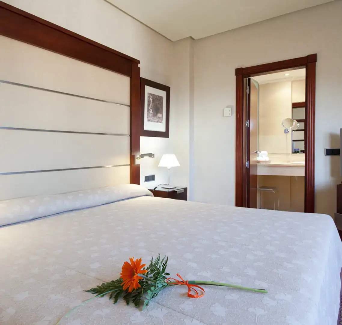 Cama con flor naranja y ba&ntilde;o al fondo en una habitaci&oacute;n elegante.