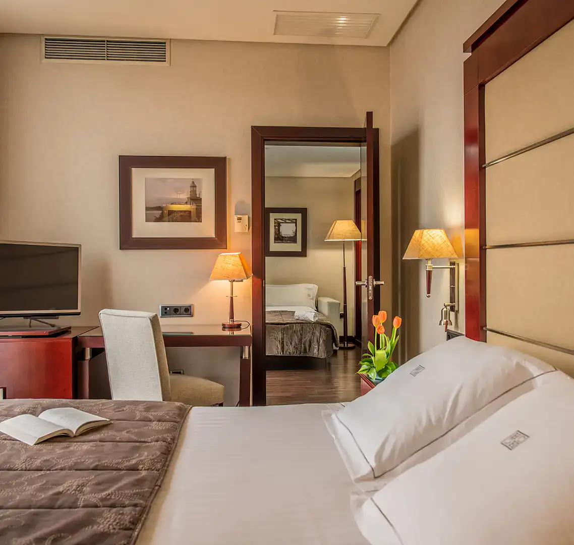 Habitaci&oacute;n de hotel moderna con escritorio, cama y l&aacute;mparas c&aacute;lidas.