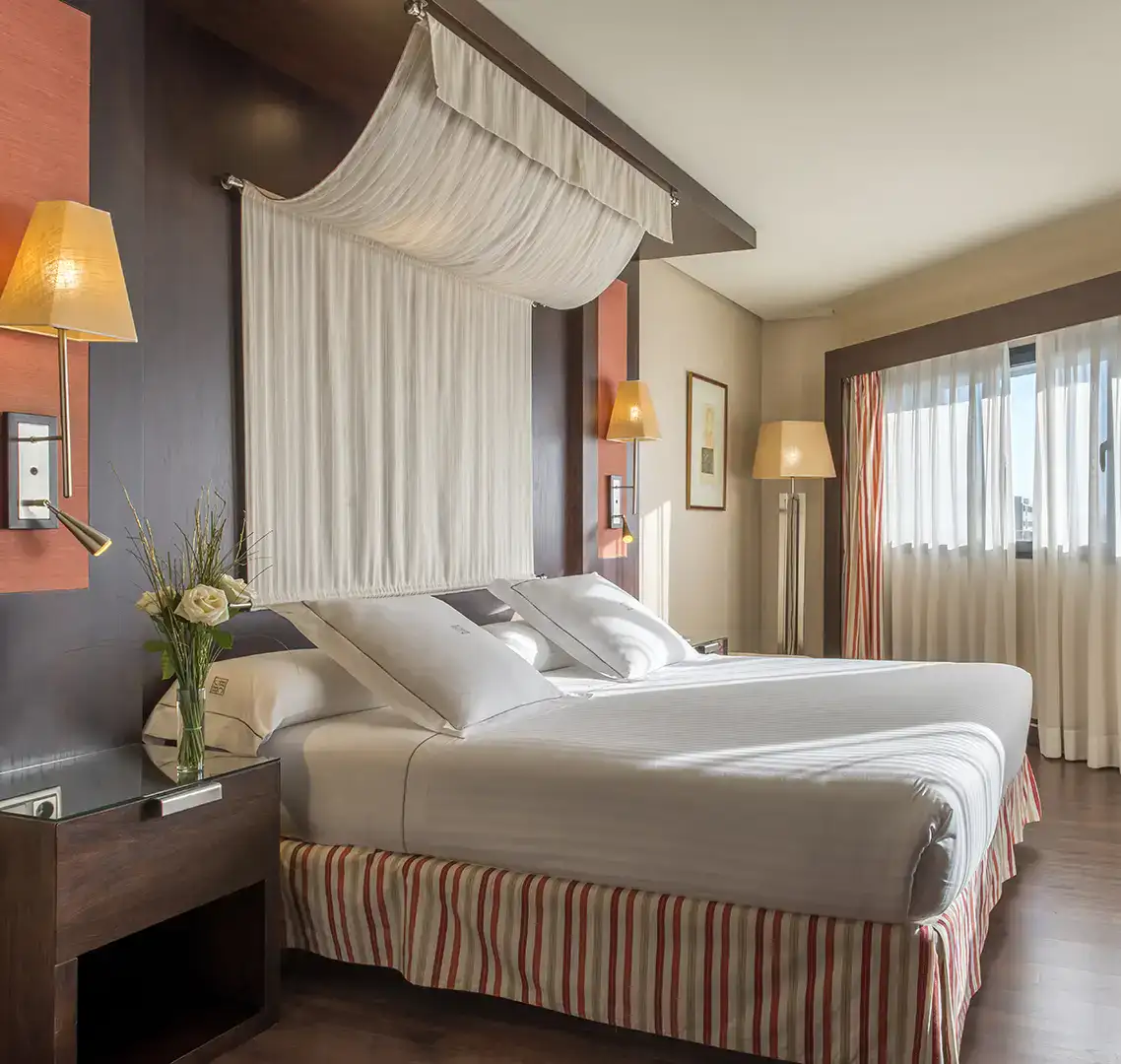 Habitaci&oacute;n de hotel con cama doble, luz natural y decoraci&oacute;n elegante.