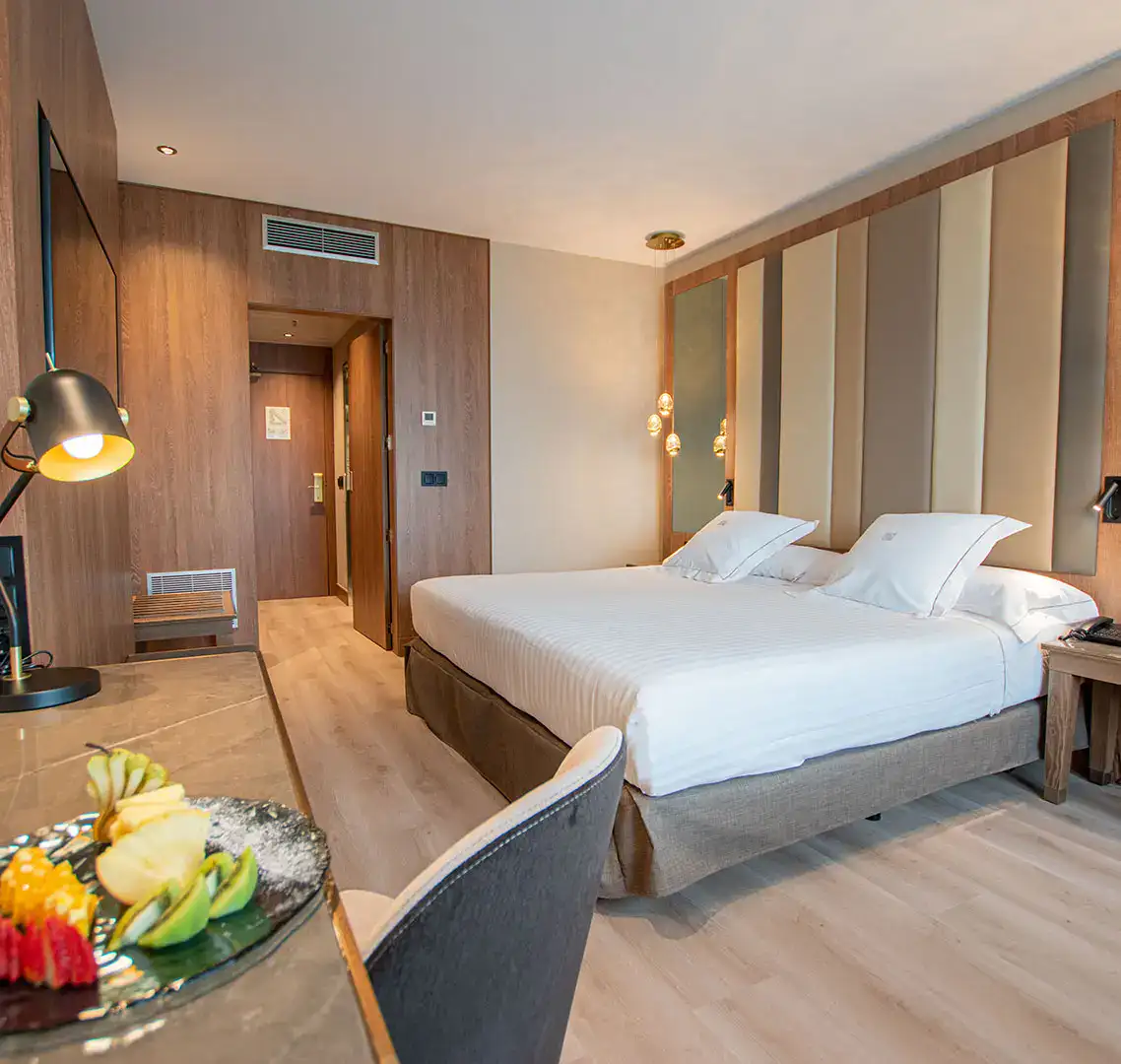 Habitai&oacute;n de hotel moderna con cama doble y plato de frutas sobre el escritorio.