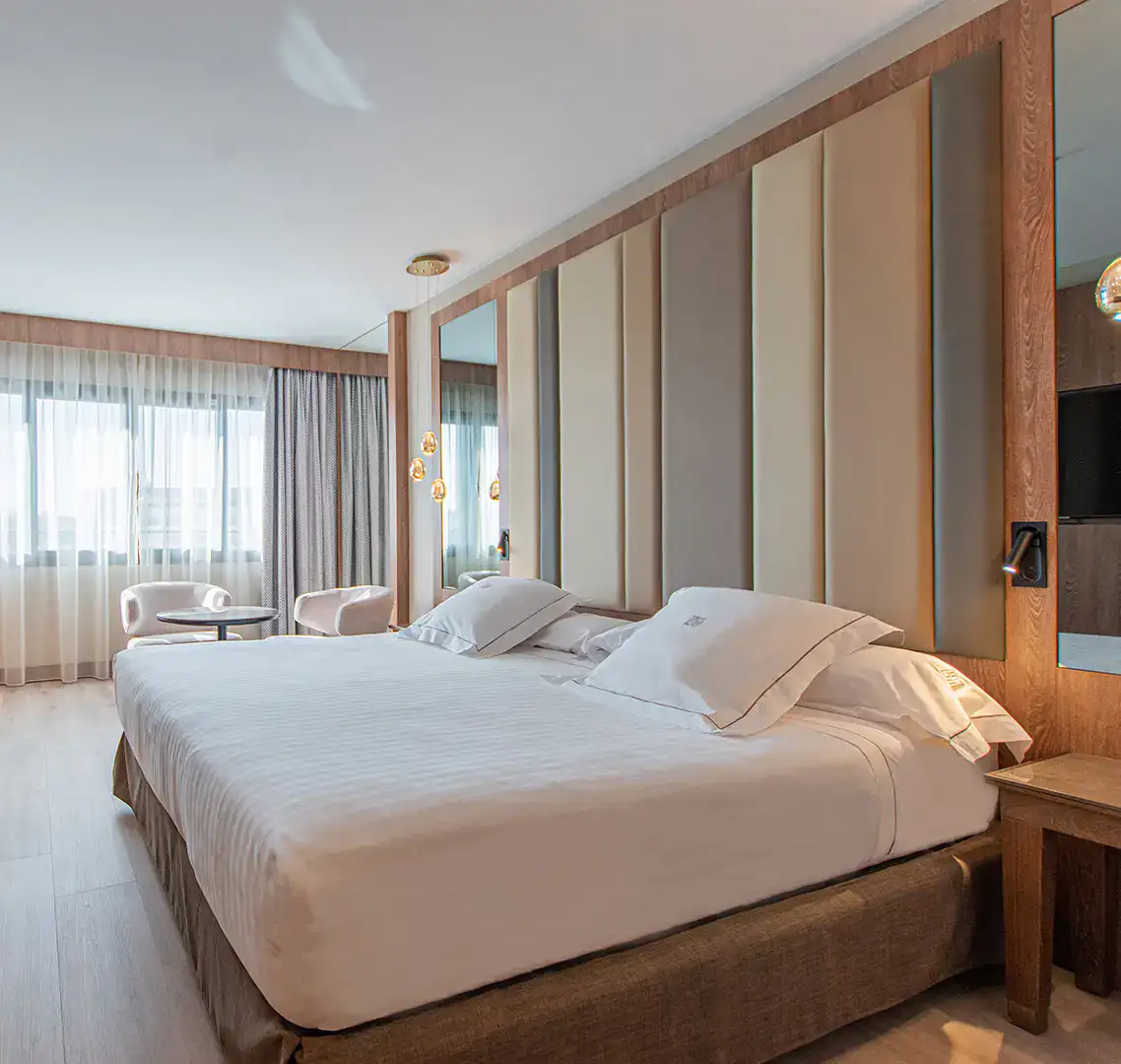 Habitaci&oacute;n de hotel moderna con cama doble y ventanales amplios.