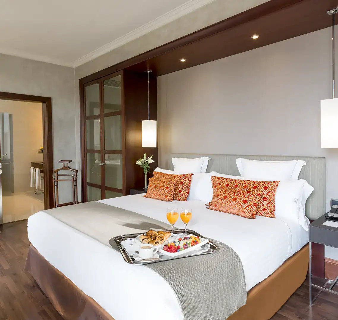 Cama con bandeja de desayuno, cojines decorativos y luz suave.