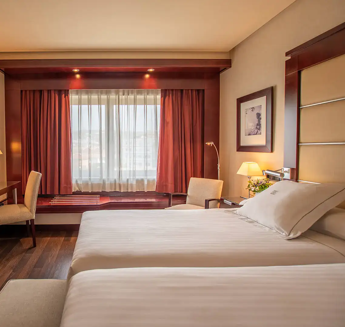 Habitaci&oacute;n de hotel con dos camas, ventana y decoraci&oacute;n elegante.