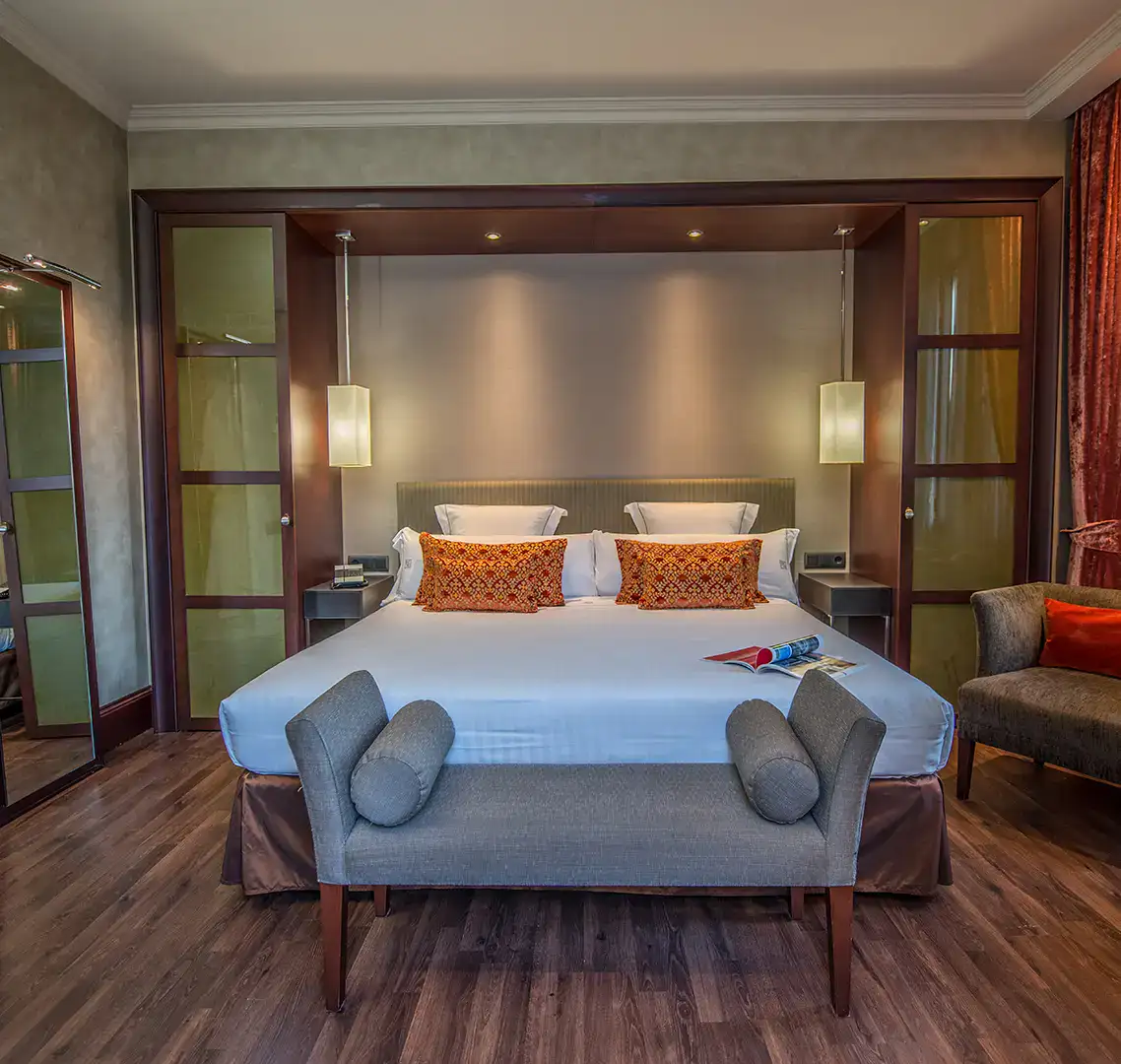 Habitaci&oacute;n moderna con cama doble, cojines naranjas y sof&aacute; gris.