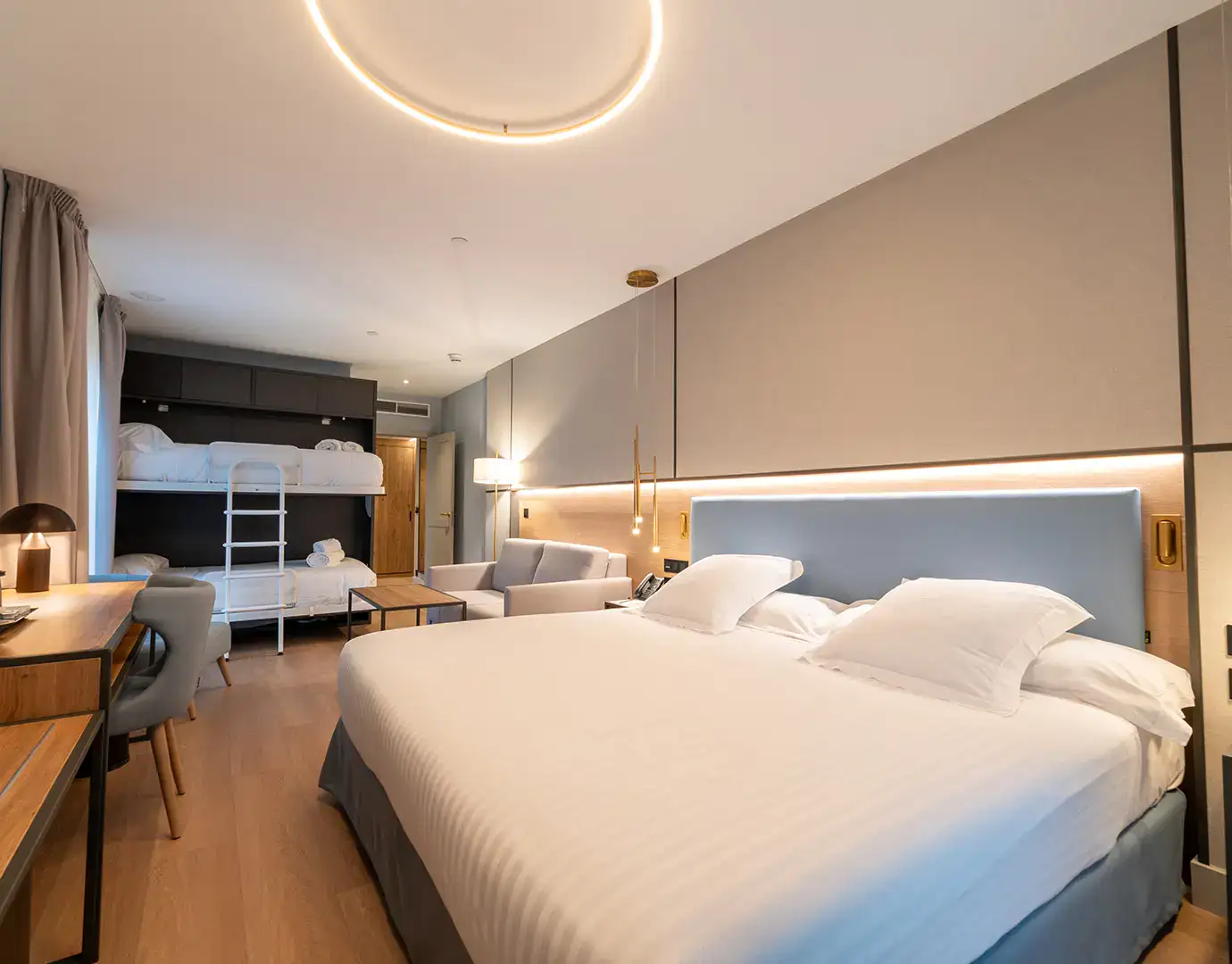 Habitaci&oacute;n moderna con cama doble, litera, sof&aacute; y escritorio.