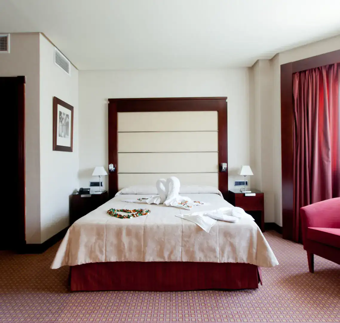 Habitaci&oacute;n de hotel con cama, decoraci&oacute;n de toallas y cortinas rojas.