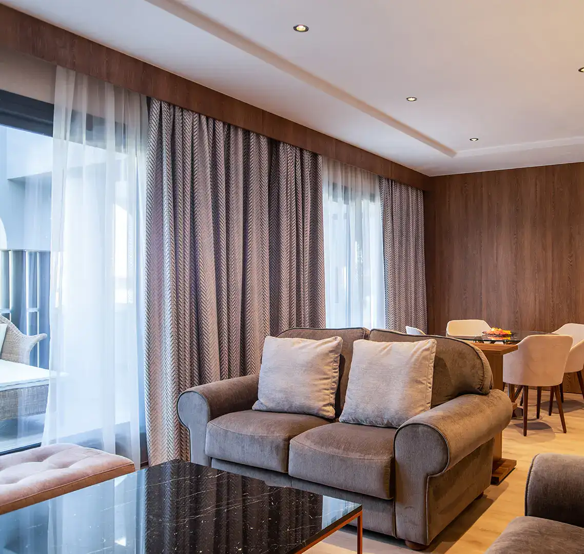 Sala moderna con sof&aacute; gris, mesa de m&aacute;rmol y cortinas largas.