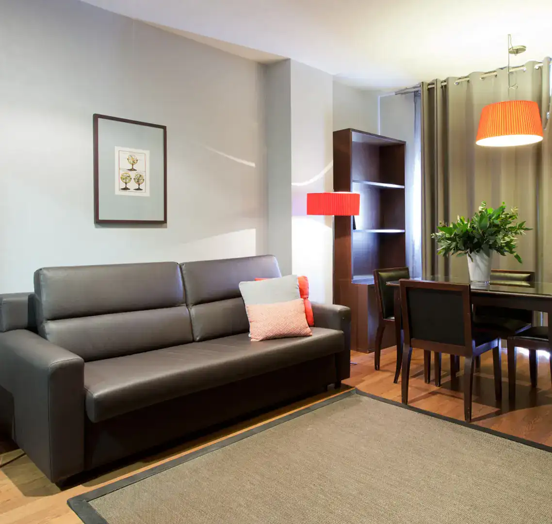 Sala moderna con sof&aacute; gris, mesa de comedor y l&aacute;mpara roja.