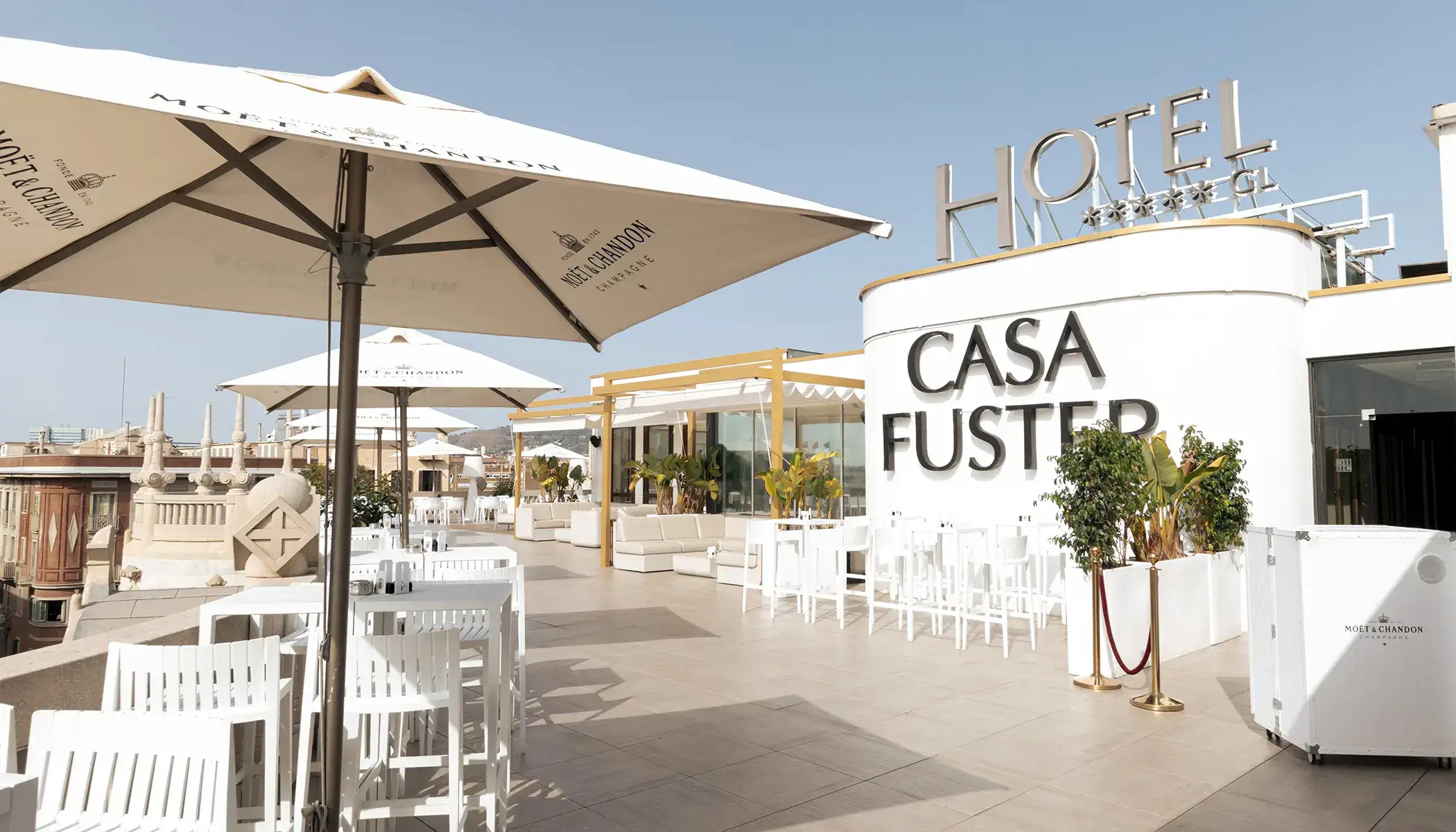 Terraza de hotel con sombrillas y muebles blancos, bajo un cielo despejado.