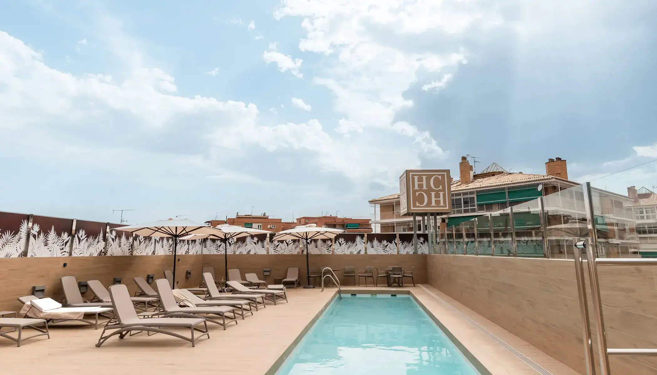 Piscina con tumbonas y sombrillas en una terraza bajo un cielo nublado.