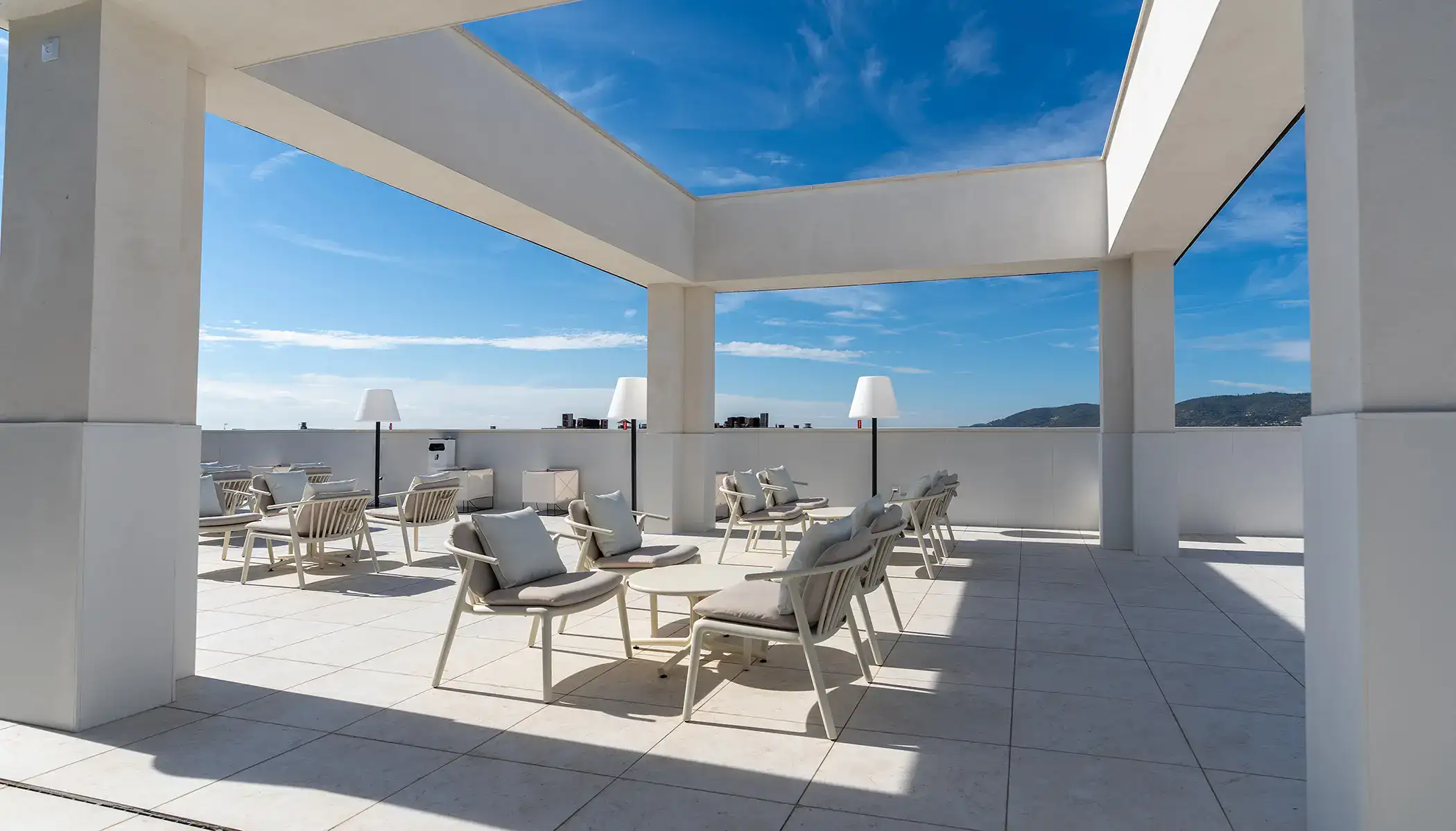 Terraza moderna con sillas y mesas bajo un cielo azul claro.